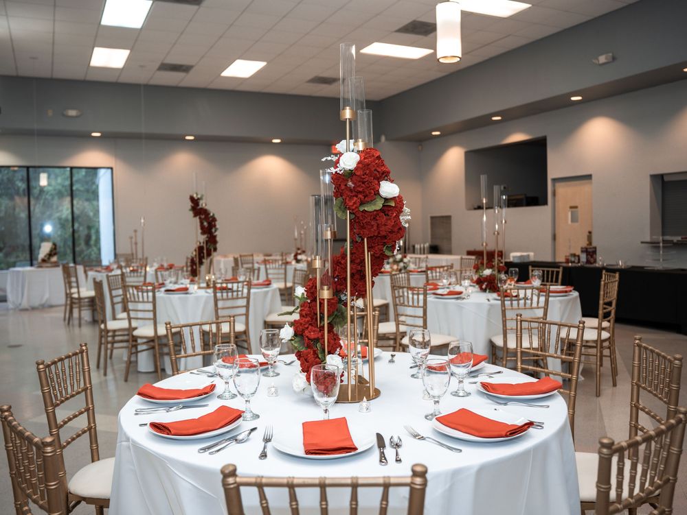 Elegant wedding reception setup with round tables, gold chiavari chairs, and tall red floral centerpieces in a modern venue in Tampa Florida