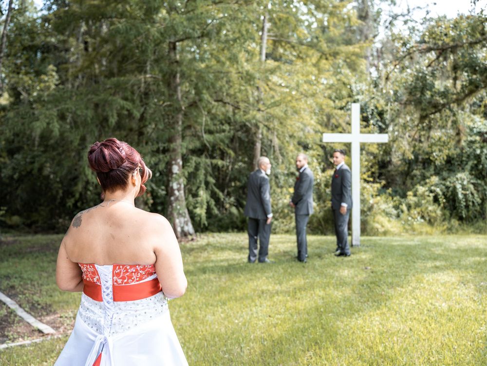 A wedding ceremony takes place outdoors with a white cross and trees in the background in Tampa Florida