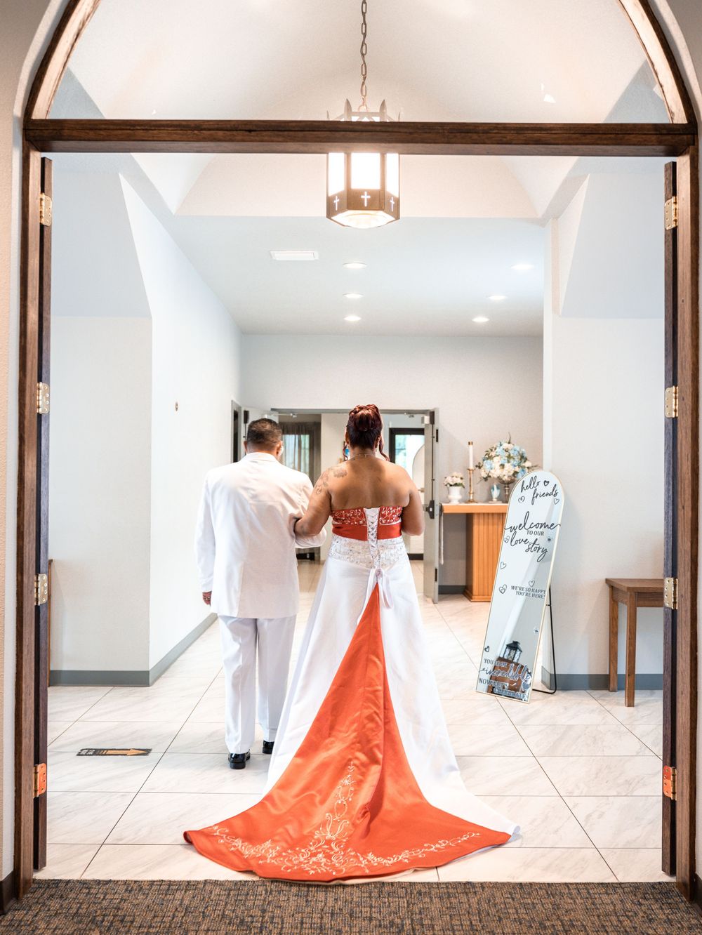 A bride in a white dress with a striking coral-colored train walks down a bright church hallway in Tampa Florida