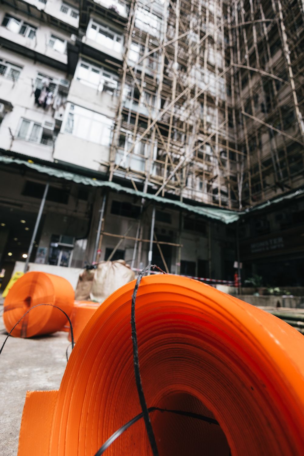 Orange plastic rolls on ground at urban construction site with bamboo scaffolding and apartment building.