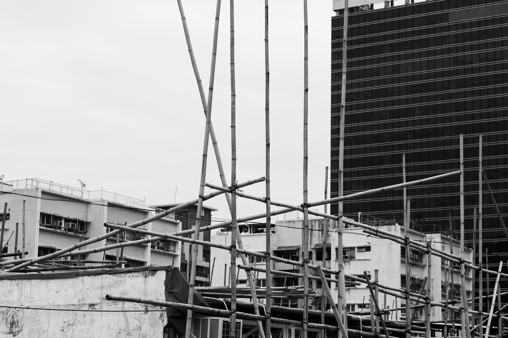 Black and white photo of construction scaffolding with a modern skyscraper in the background.