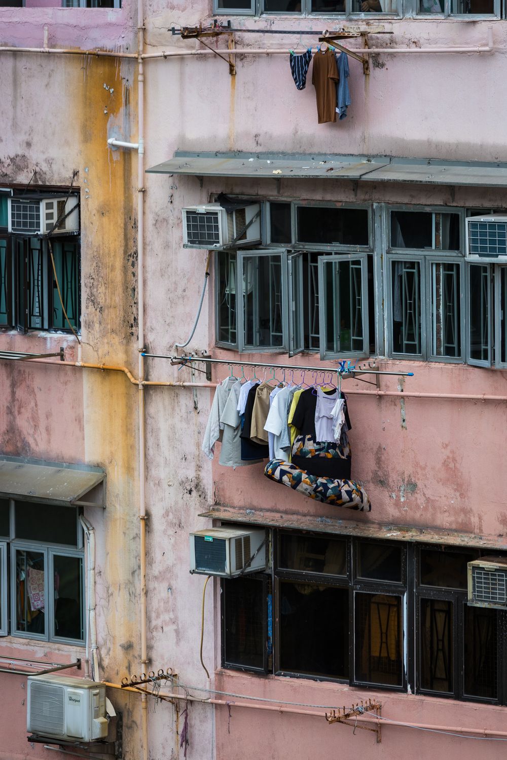 Weathered pink apartment building exterior with laundry hanging on clotheslines and air conditioning units.