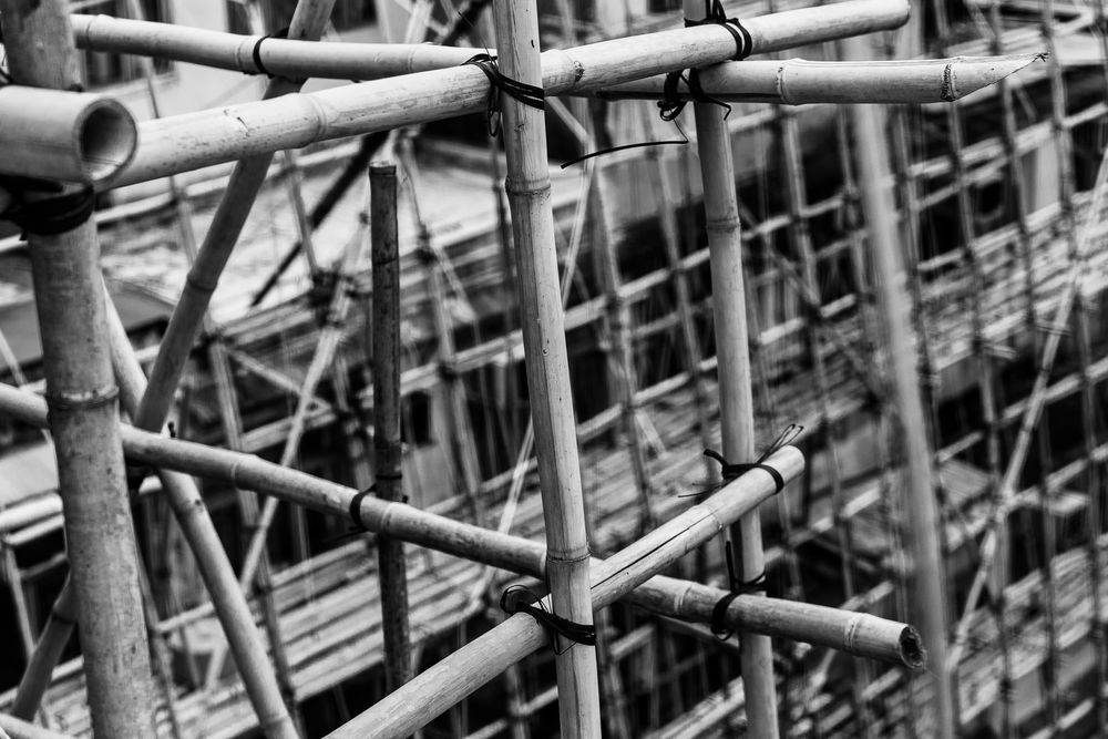 Close-up black and white photo of interlocking bamboo scaffolding poles at a construction site.