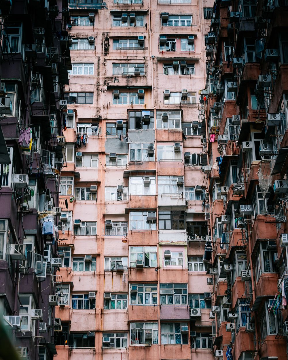 Densely packed pink Hong Kong apartment building facade covered with air conditioning units and balconies.