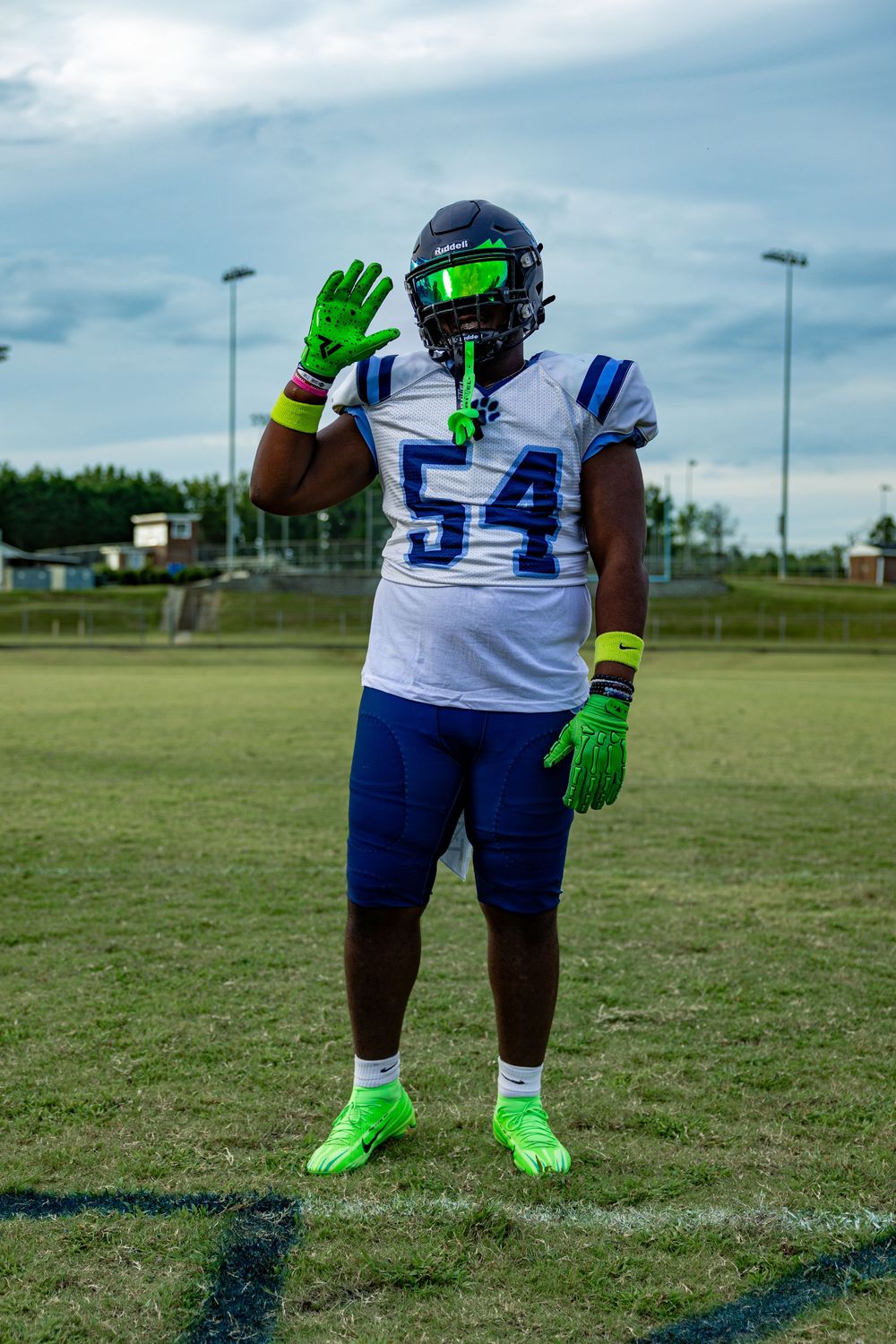 Football player wearing jersey number 54 in white and blue uniform with bright green gloves and cleats on field.