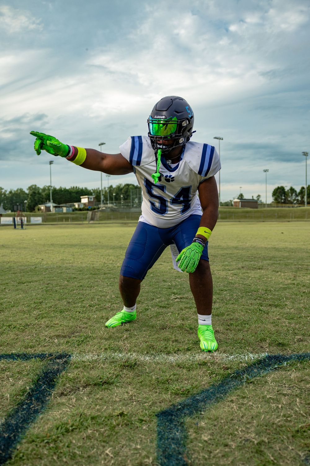 Football player in blue and white uniform demonstrates diving catch sequence on grass field with neon green gloves.
