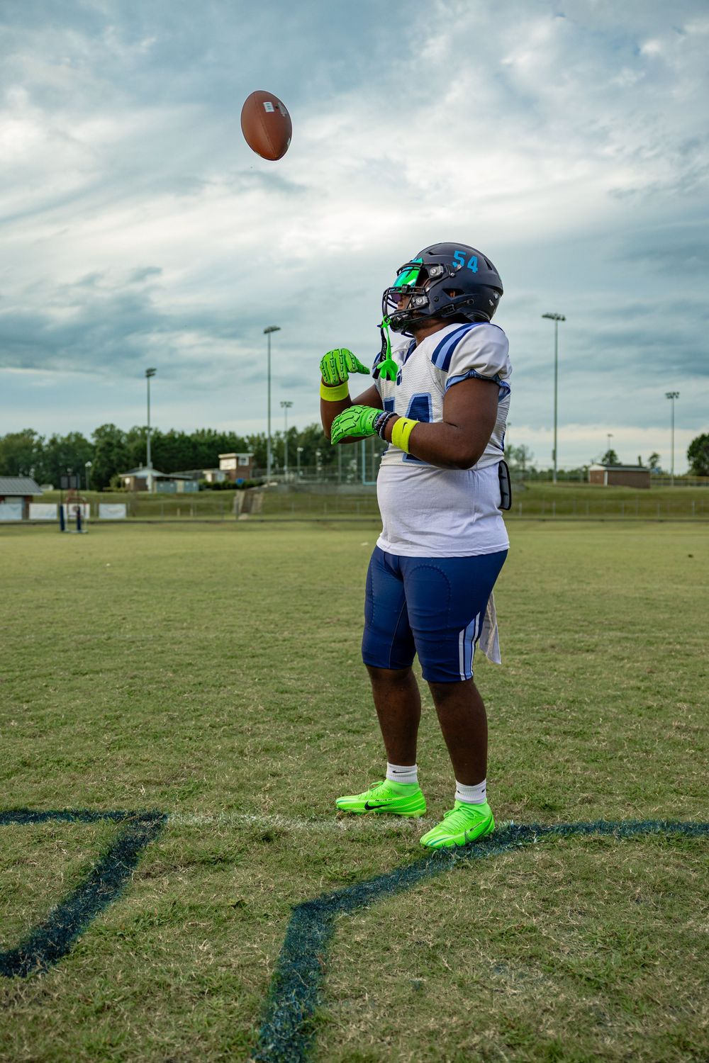 Football player catching ball on field while wearing bright green gloves and white uniform with number 54.