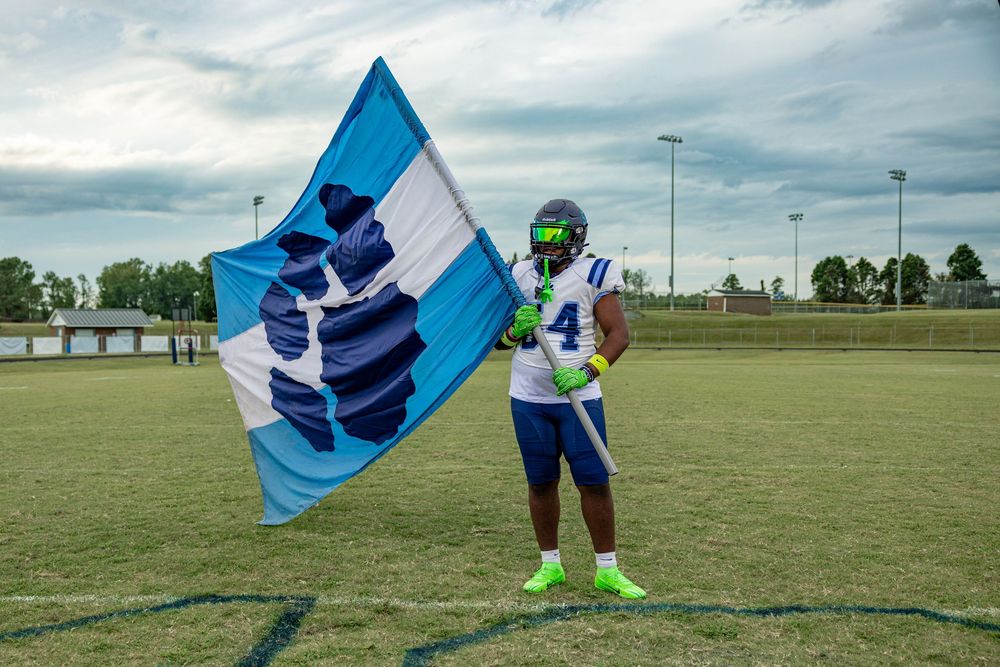 Football player waves blue team flag on sunny field during practice session.