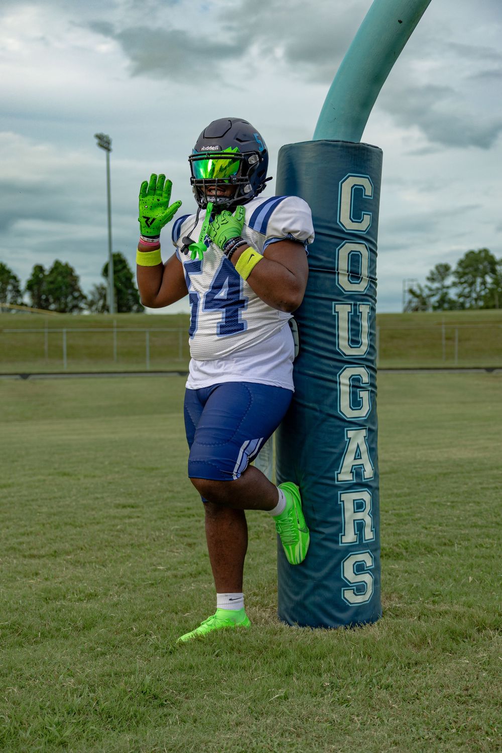 Football player performs training exercises with a blue tackling dummy wearing bright green gloves on a field.