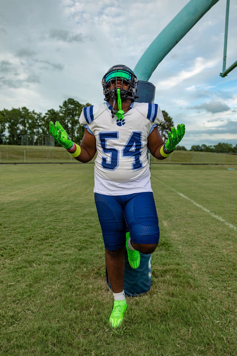 Football player in uniform number 54 poses on field wearing bright green gloves and cleats.