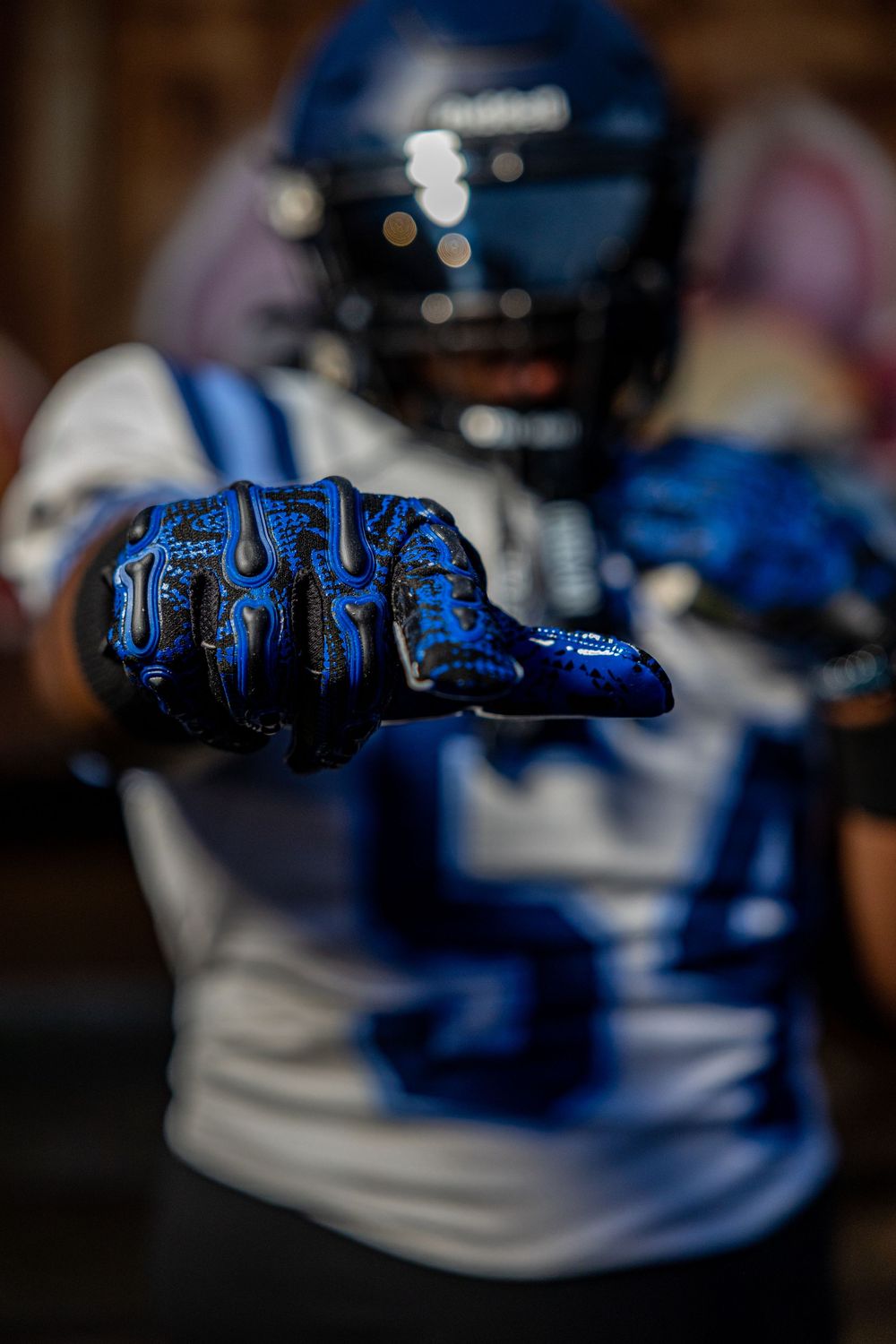 Close-up of player's hand in blue football glove pointing forward against dark background.