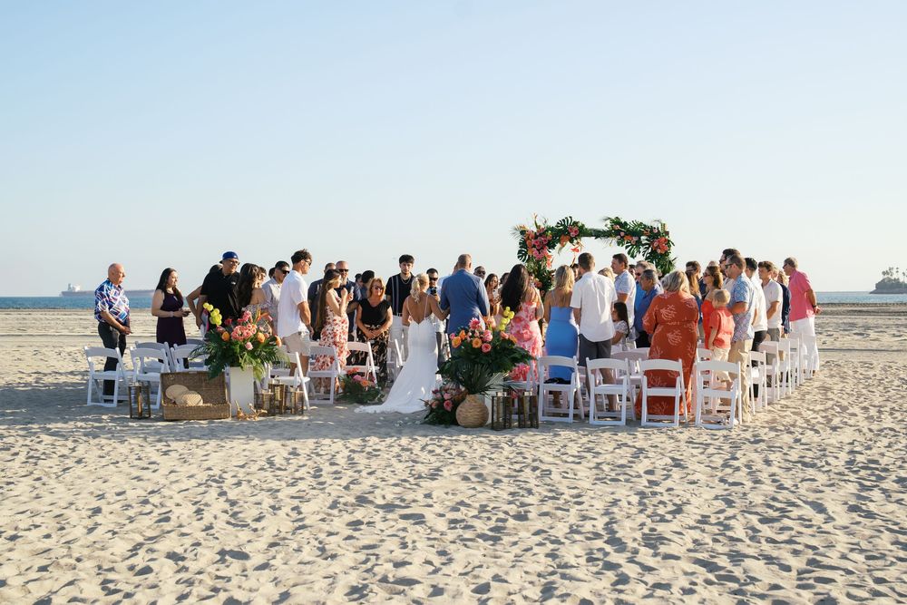 Beach wedding ceremony setup with white chairs and tropical floral decorations arranged in rows on pristine sand.