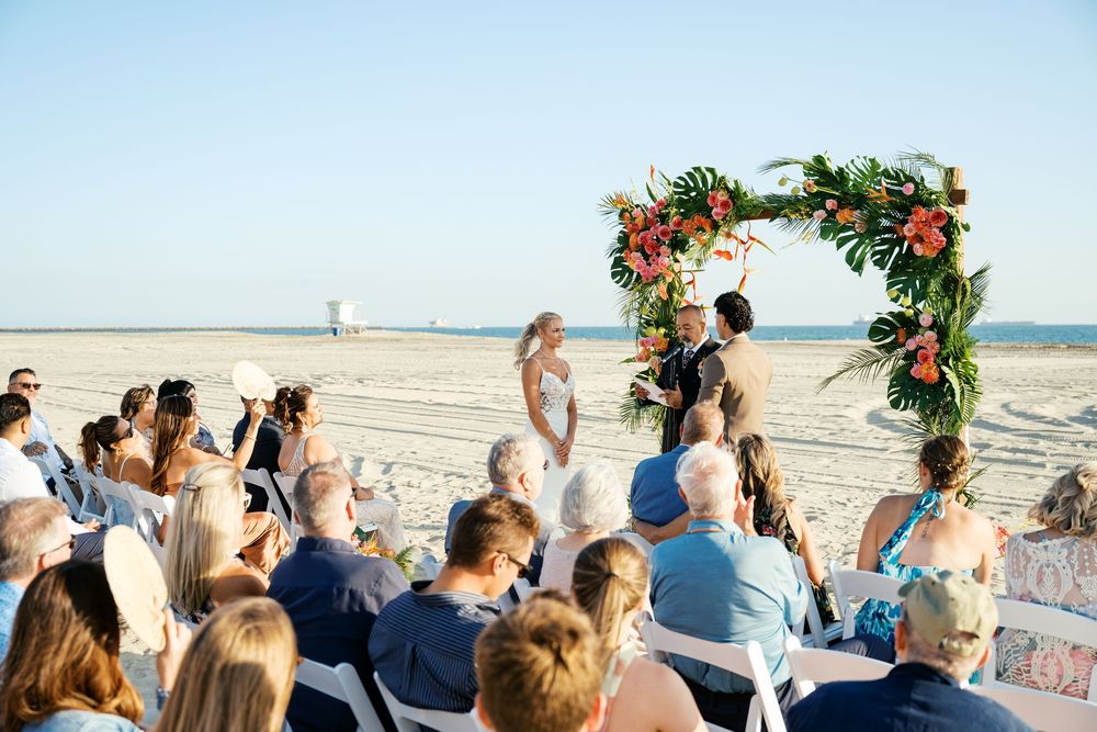 Wedding guests gathered on a beach with ocean backdrop watching outdoor ceremony.