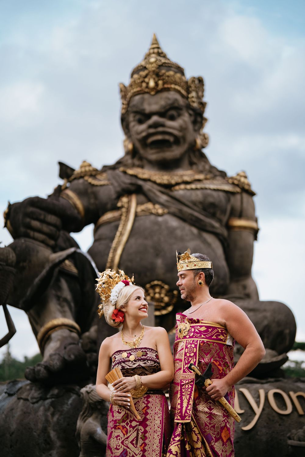 Traditional Balinese ceremony attire against backdrop of stone guardian statues.