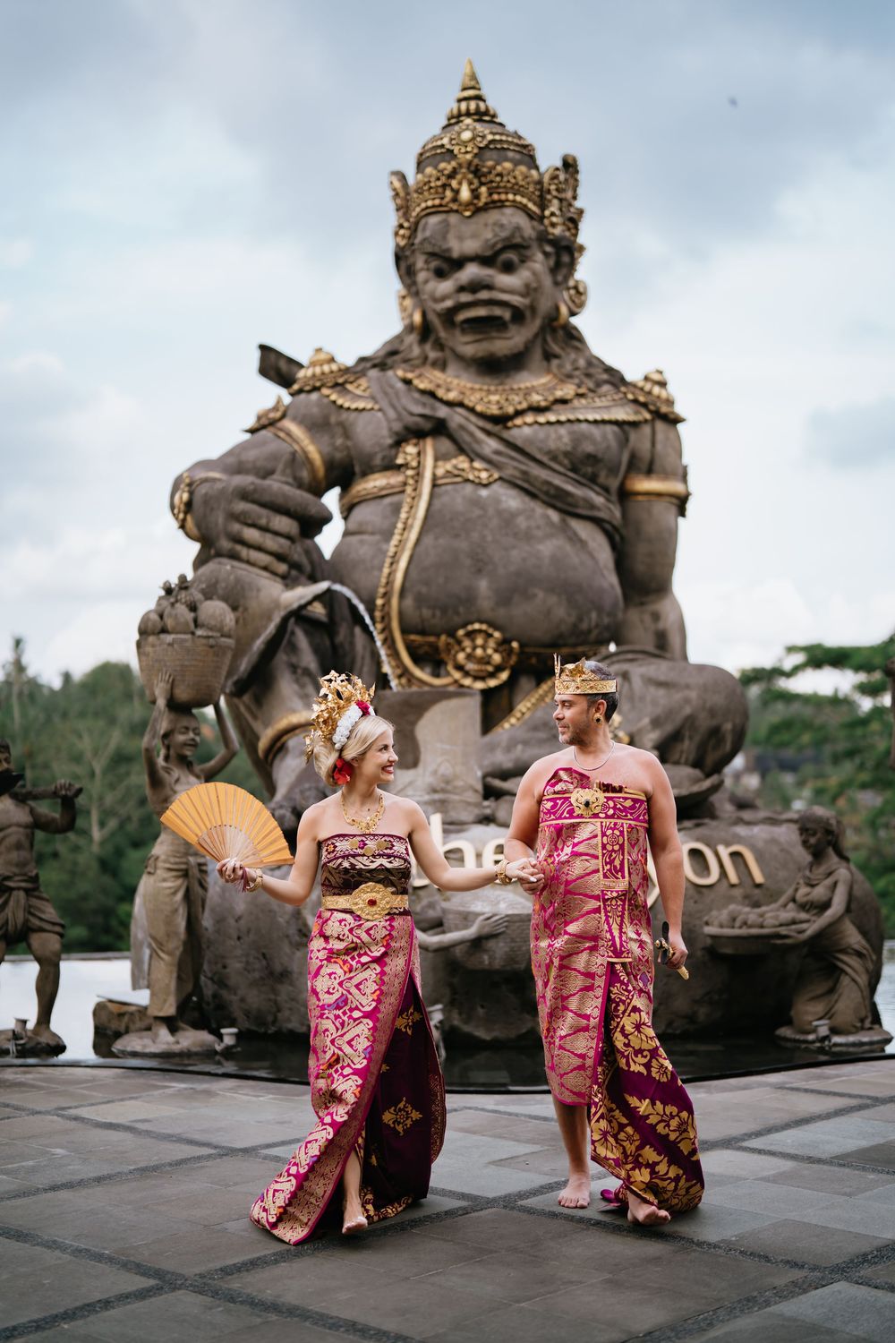Traditional Balinese wedding photoshoot with ancient stone statues in background.