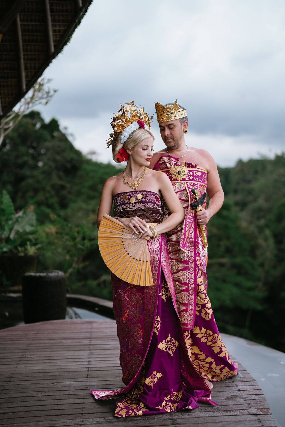 Dancers in ornate Balinese attire with gold headdresses perform on an outdoor wooden stage.