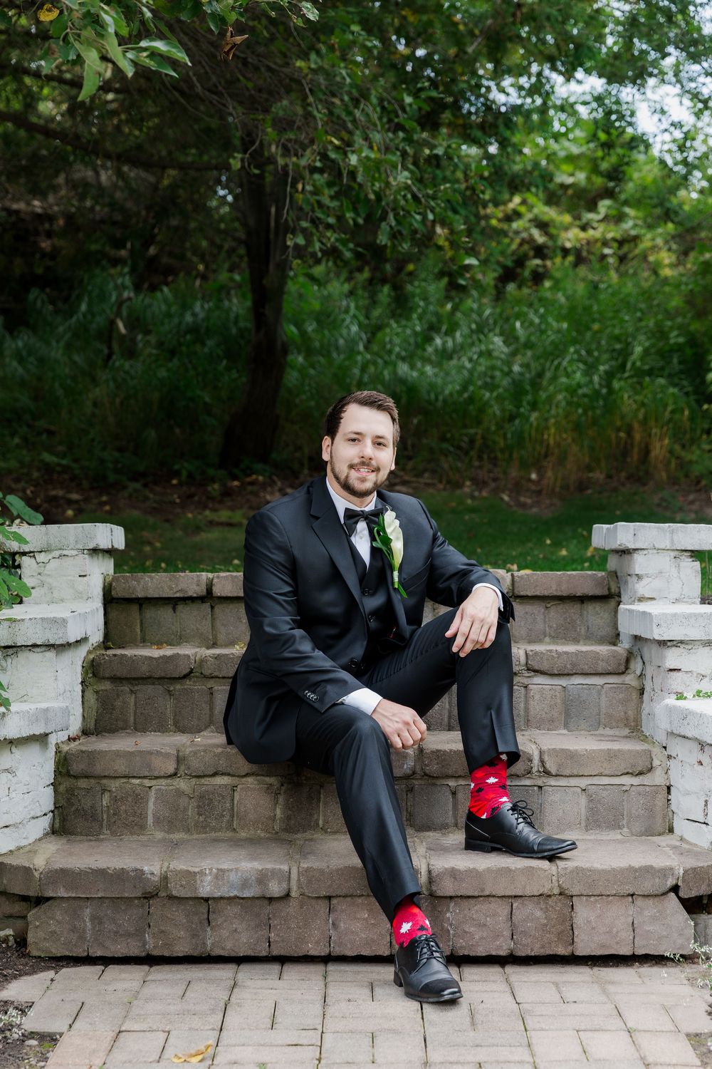 Groom sits casually on stone steps showing off his colorful socks in the garden at The Wren House in St. Jacobs, Ontario.