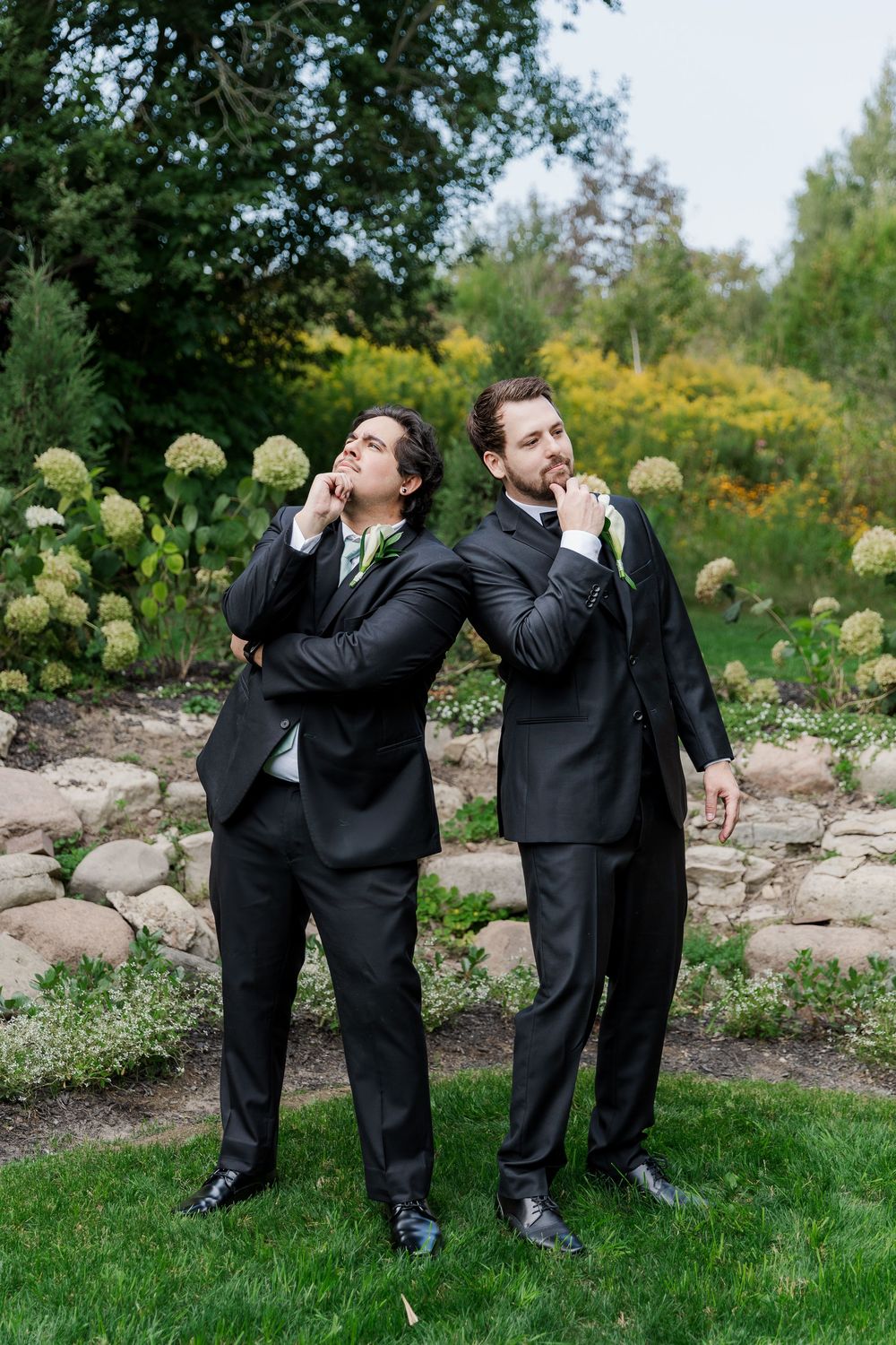 Wedding party members strike fun poses in a garden landscape with hydrangeas and stone features at The Wren House in St. Jacobs, Ontario.