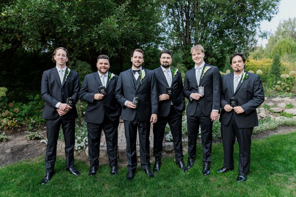 Groom and his groomsmen pose with their wedding party gifts in the garden at The Wren House in St. Jacobs, Ontario.