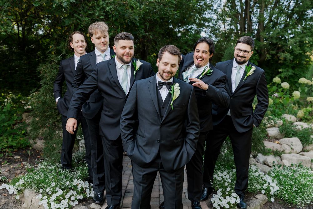 Groomsmen surround the groom and congratulate him in the gardens at The Wren House in St. Jacobs, Ontario.