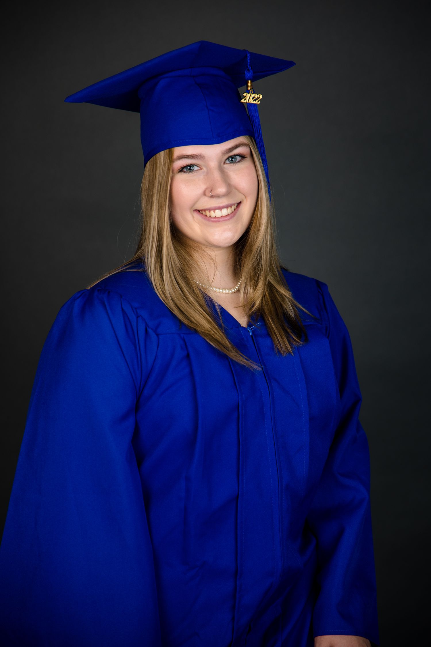 Graduate student in bright red graduation gown holds their diploma against blurred outdoor background.