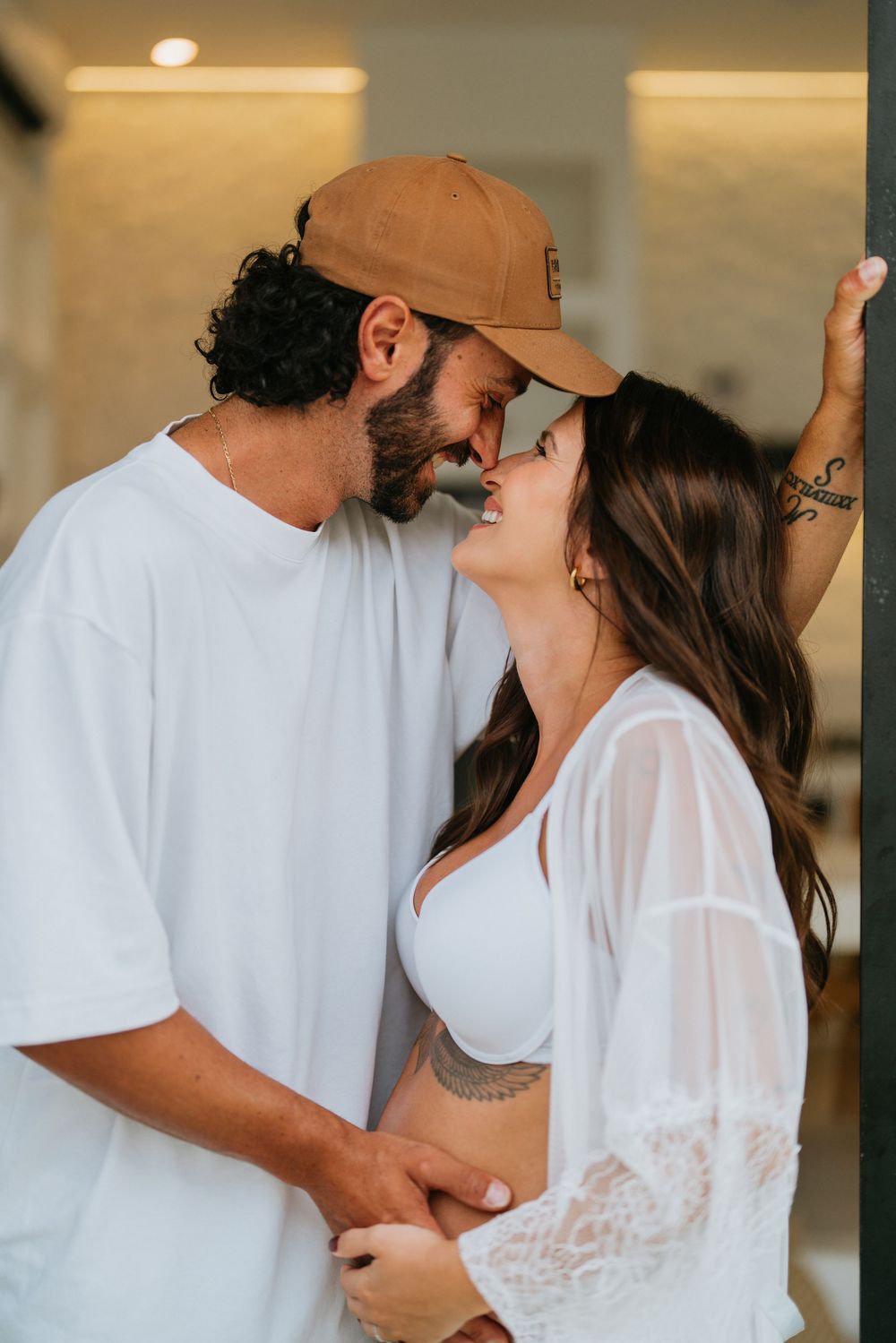 Intimate couple's photoshoot in casual white outfits against neutral backdrop.