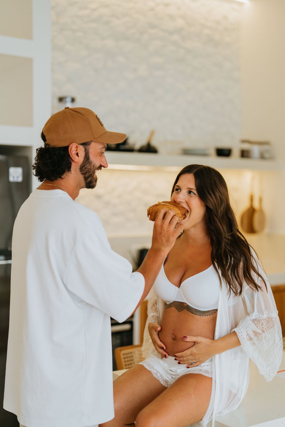Romantic couple in white loungewear sharing intimate moments in a bright modern interior.