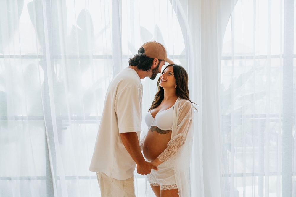 Intimate couple photoshoot with soft white curtains in the background.
