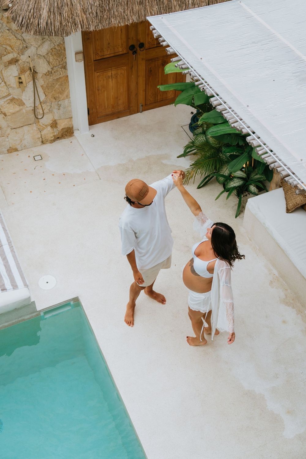Couple enjoying time together by a turquoise pool with stone and greenery backdrop.