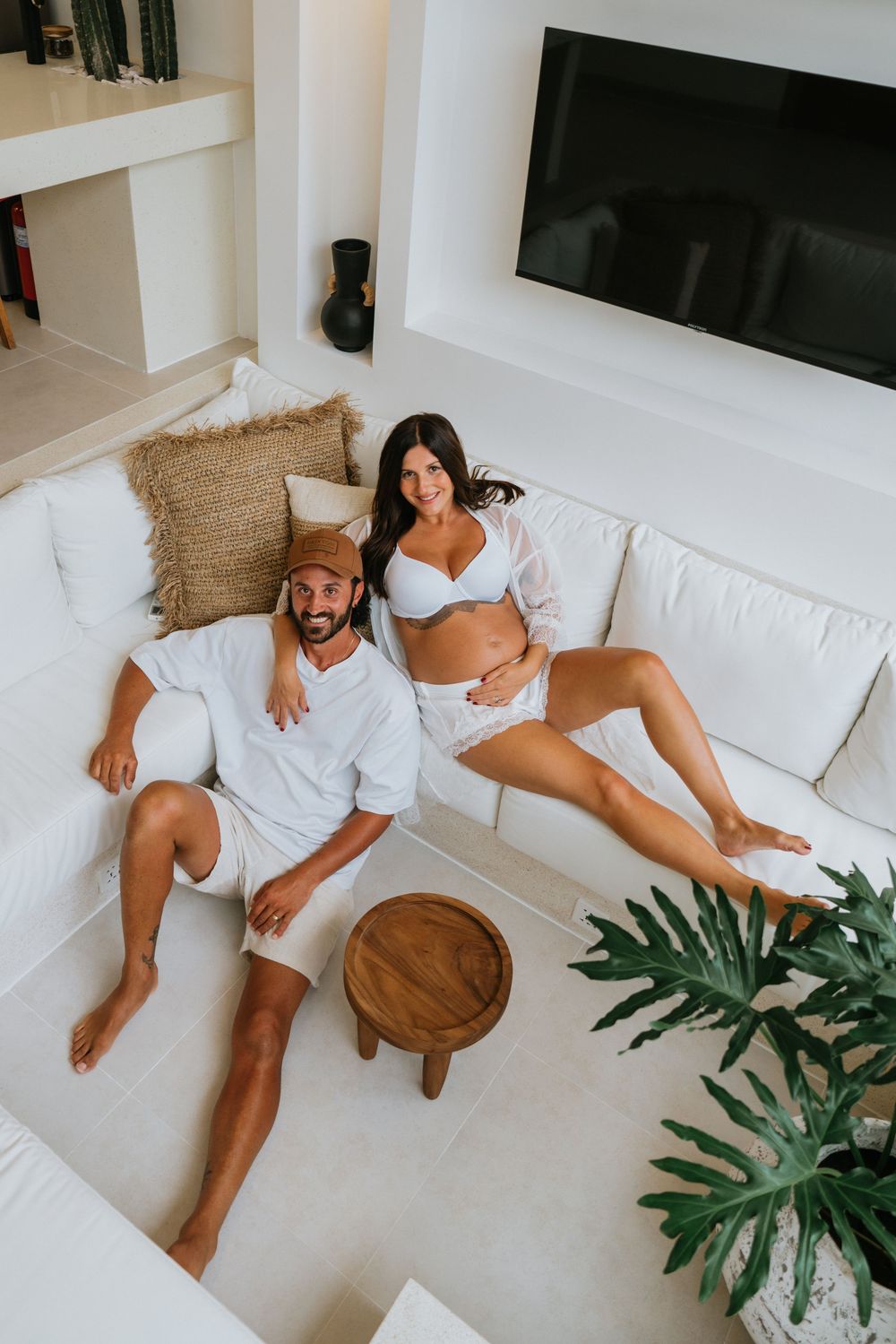 Couple lounging on white sectional sofa with tropical plants in modern interior.