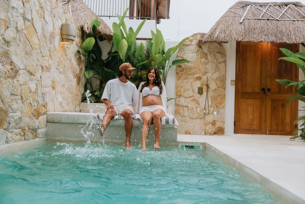 People enjoying a luxurious pool surrounded by stone walls and tropical plants at a resort.