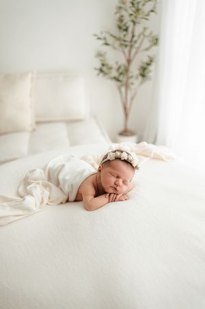 Peaceful newborn baby sleeping on soft white bedding in natural light with minimal decor.