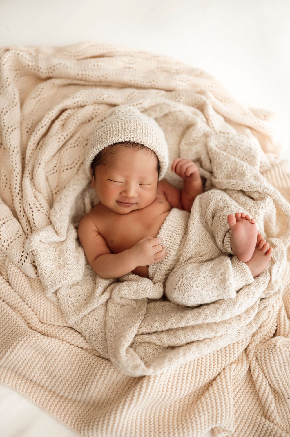 A peaceful series of photos featuring a sleeping newborn baby wrapped in a cozy cream-colored knit blanket.