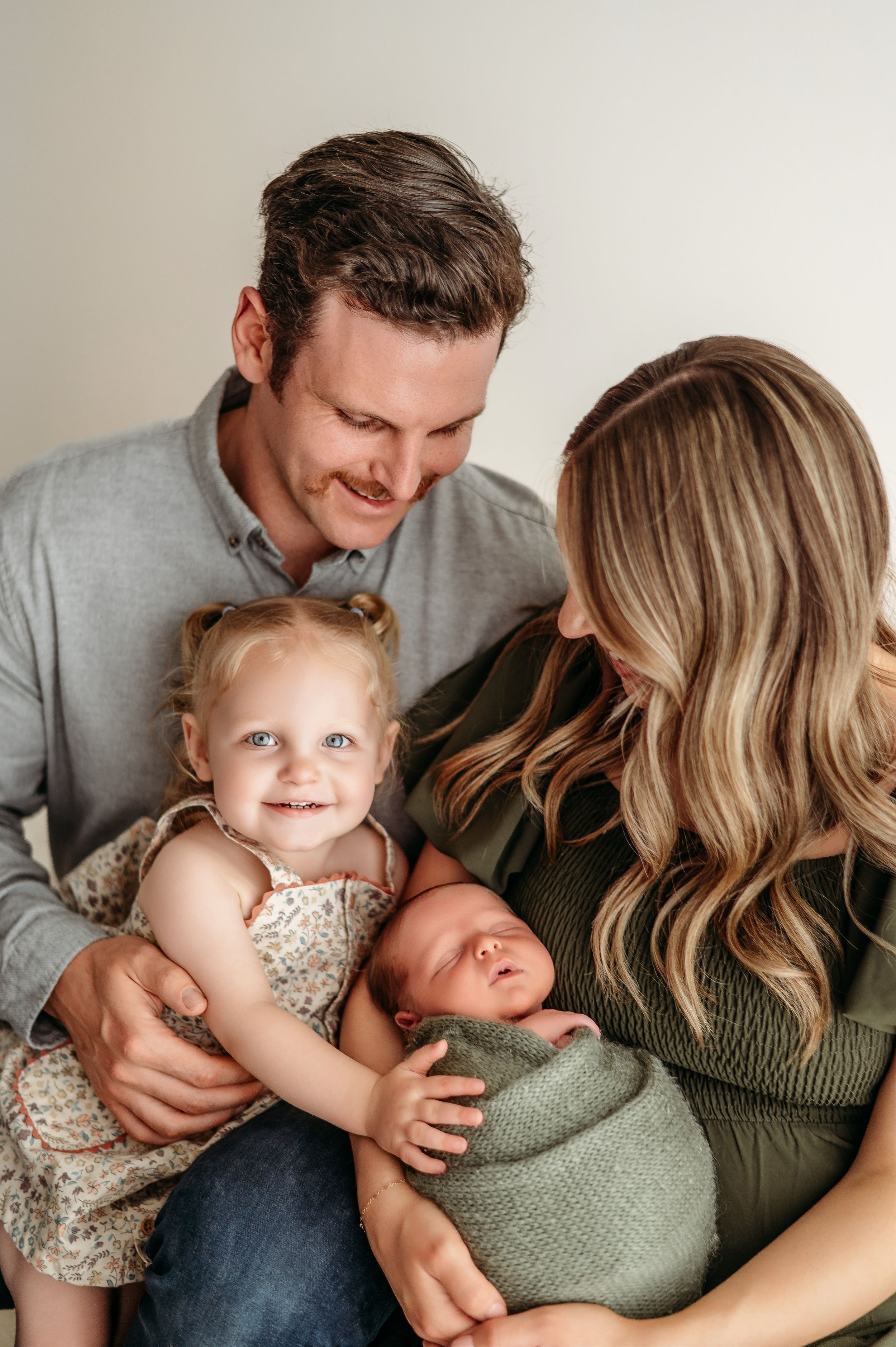 A young family shares tender moments together on a couch, dressed in green and neutral tones.