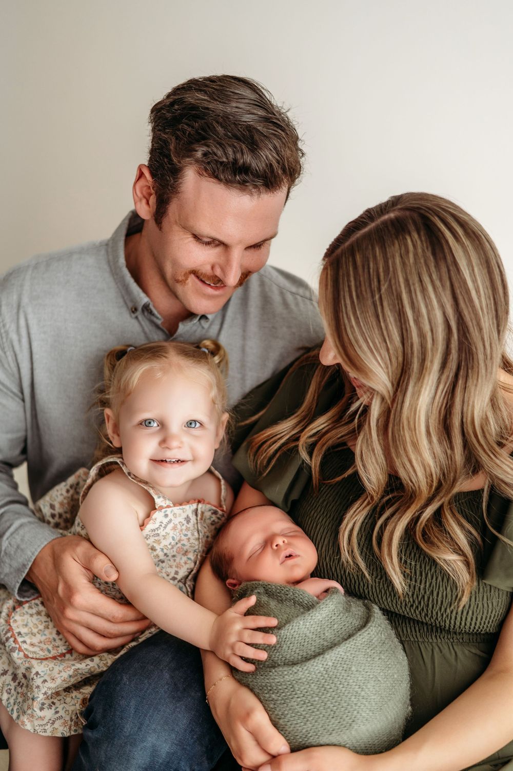 A young family shares tender moments together on a couch, dressed in green and neutral tones.