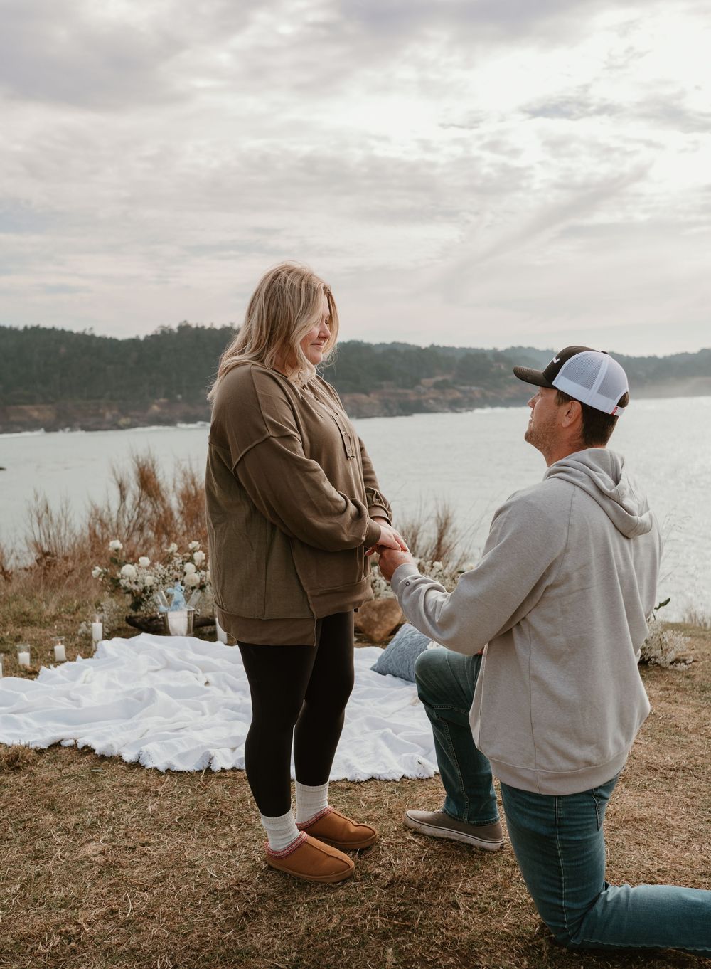 A special moment unfolds between two people on a scenic cliff overlooking a bay.