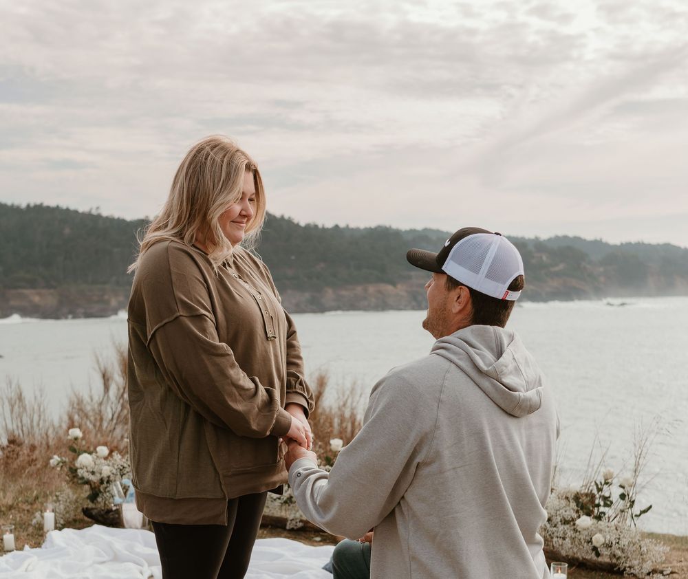 Two people share a tender moment on a coastal overlook during an overcast day.