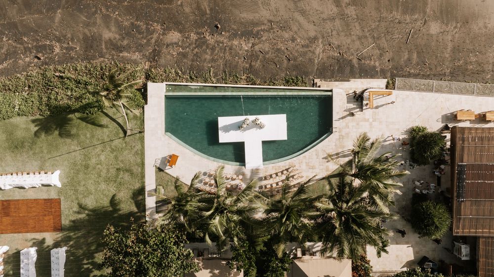 Aerial view of tropical palm trees and resort buildings along a sandy beachfront in Bali