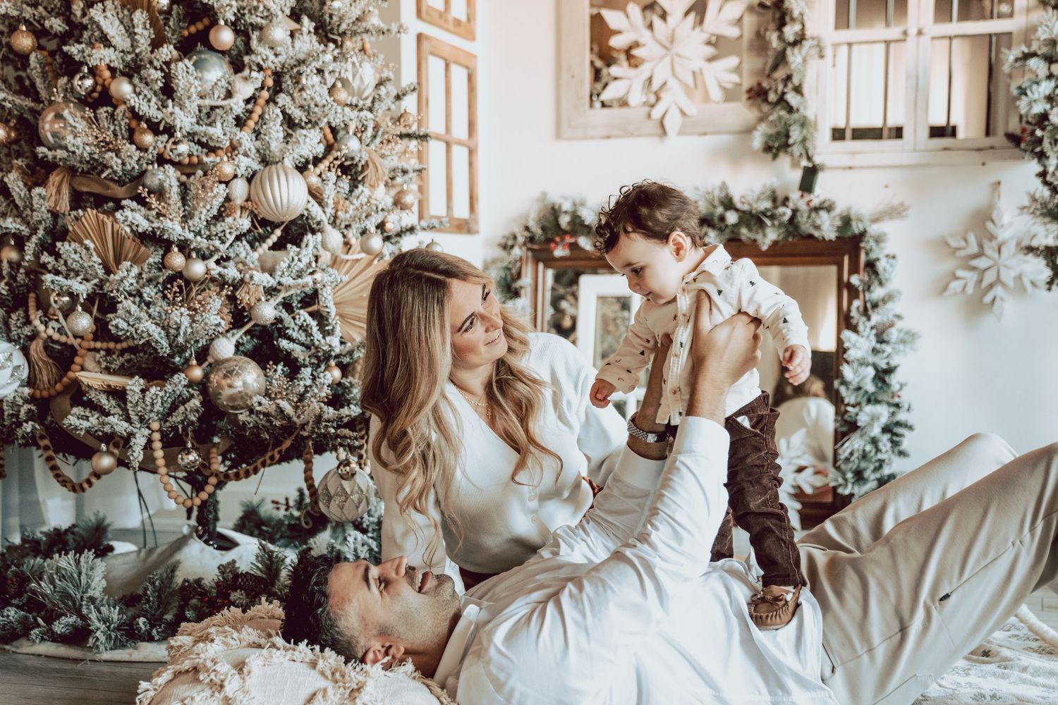 Family of 4 sitting happily  in front of an elaborate christmas tree with beautiful ornaments amongst many other holiday decorations