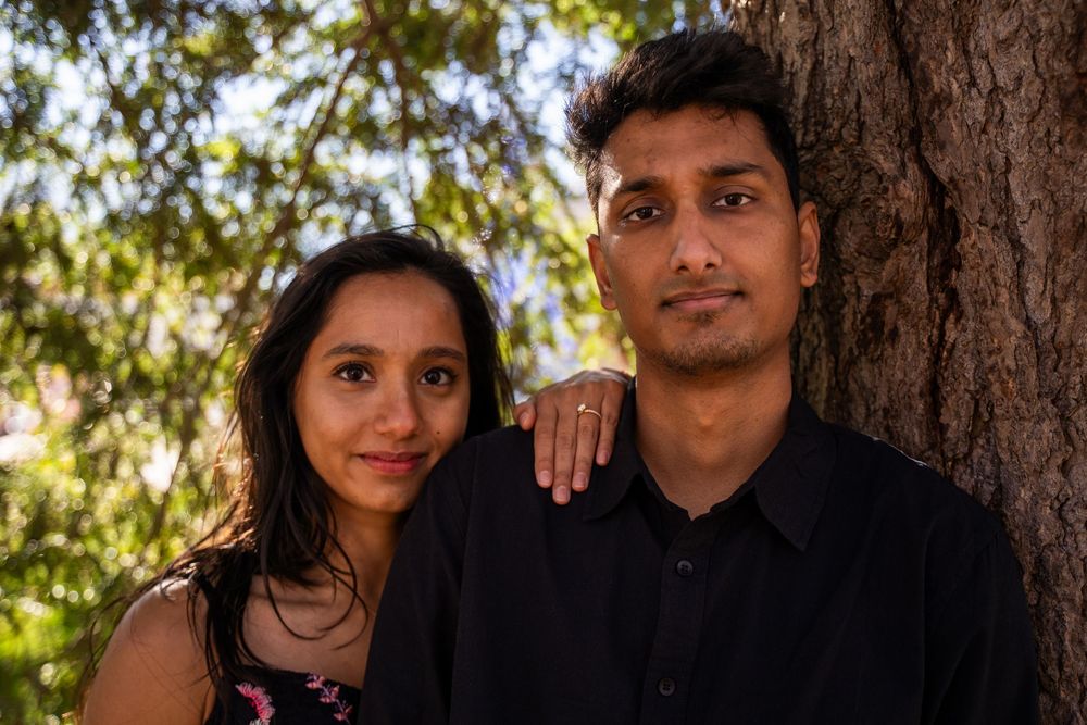 Engaged couple poses intimately together leaning against a tree trunk outdoors in natural light.