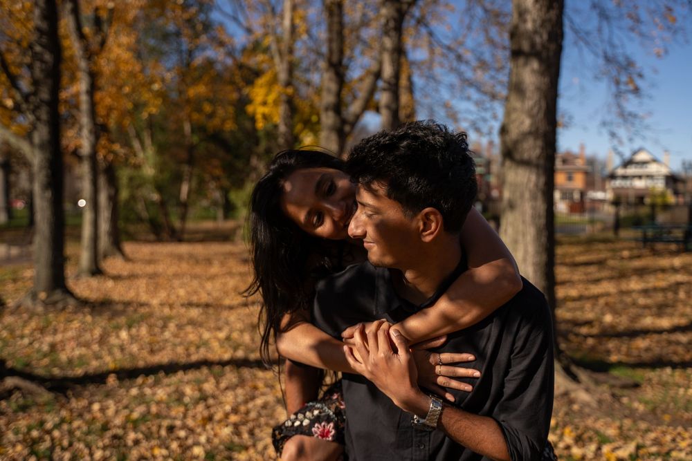 Couple embracing in autumn park with golden leaves and trees in background on a sunny fall day.