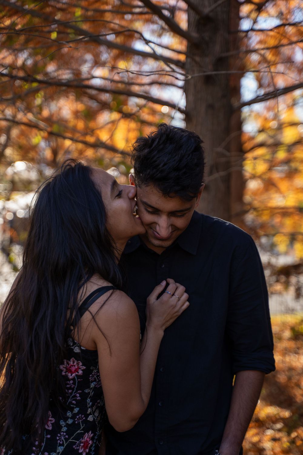 Couple sharing a romantic kiss among autumn trees with golden orange foliage in the background.