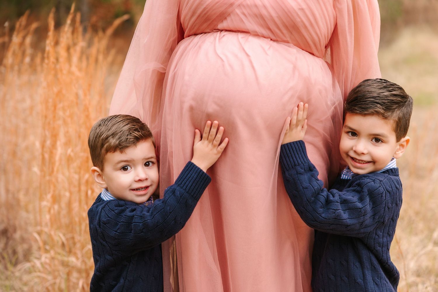 A family wearing coordinating pink and navy outfits poses together during a sunny autumn photo session in nature.
