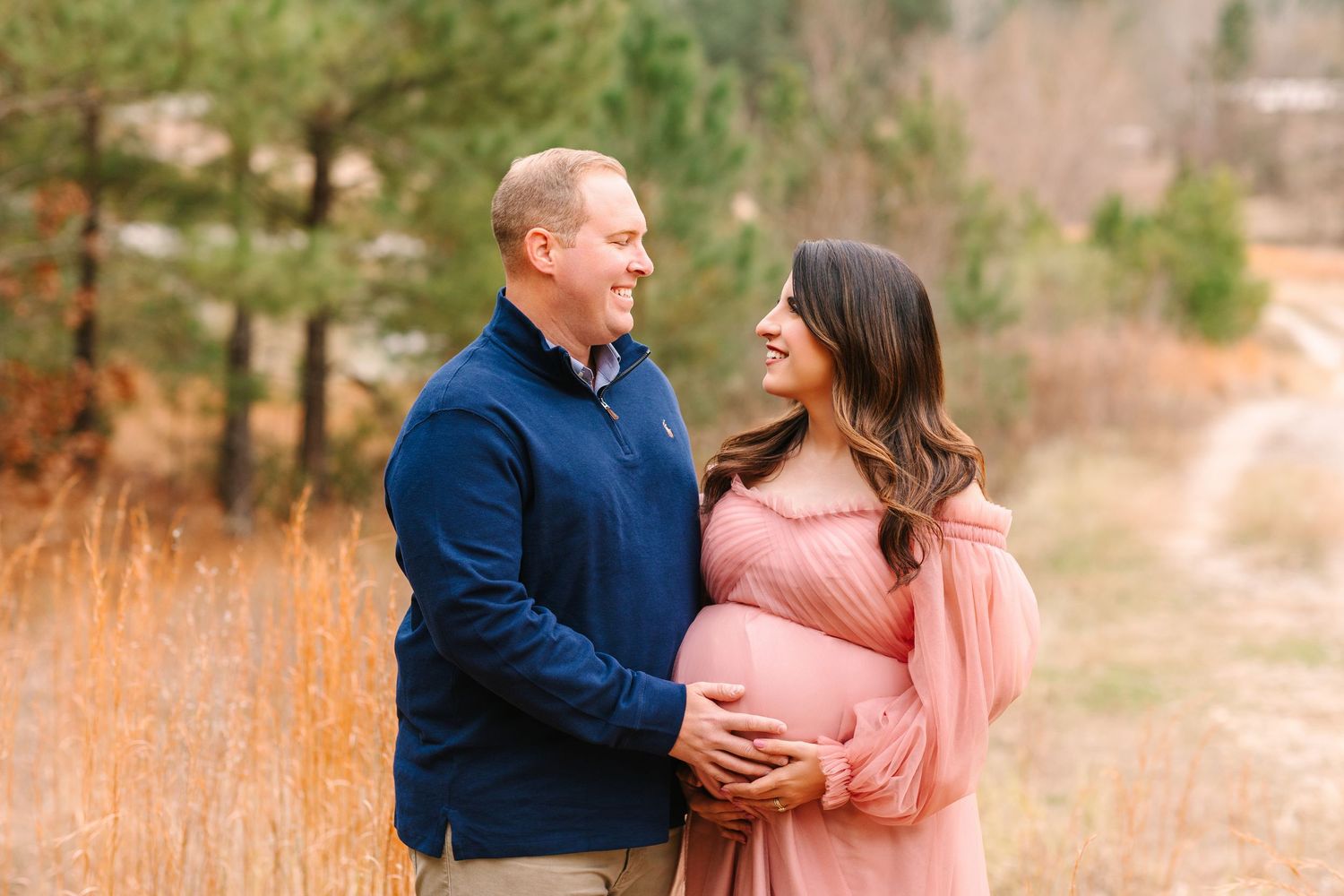 Outdoor family photo with navy and pink color scheme captures sweet moment in a natural setting with tall grass.