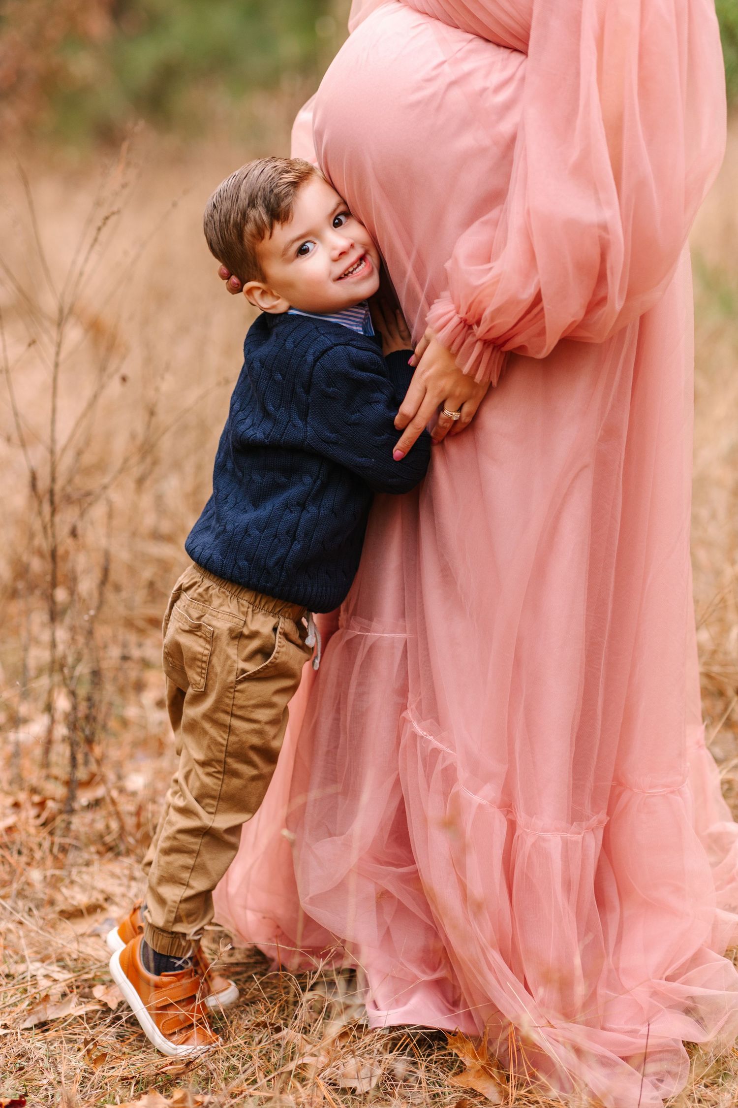 A candid moment in a field shows a small child hugging someone wearing an ethereal pink dress.