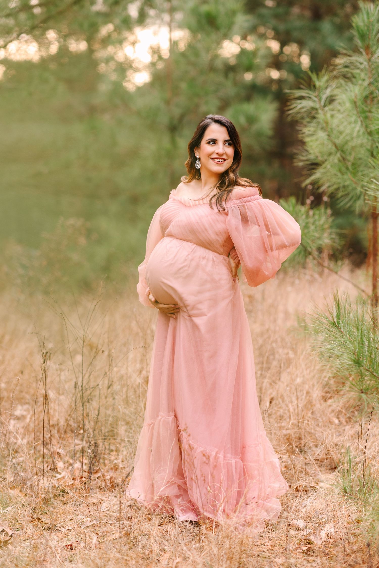 A joyful scene in golden light features someone wearing a romantic pink gown posing in tall grass.