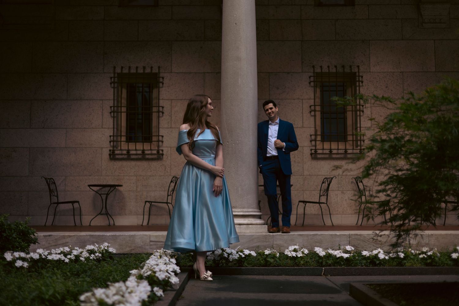 Wedding party in formal attire gathers outdoors at a grand estate venue during daytime celebration.