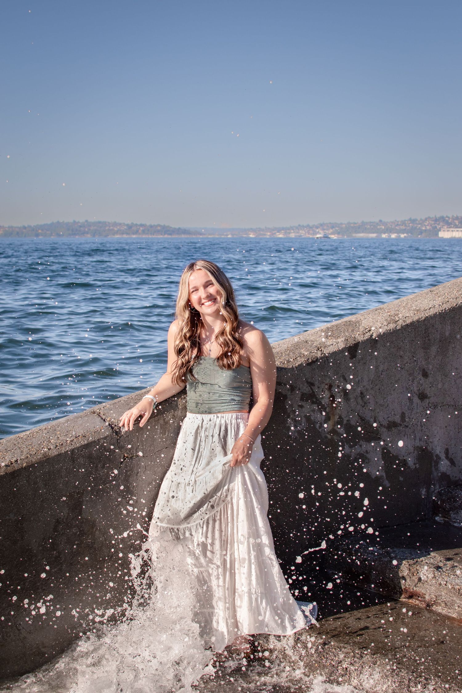 Senior girl laughing while splashing water along the seawall at Alki Beach, playful portrait.