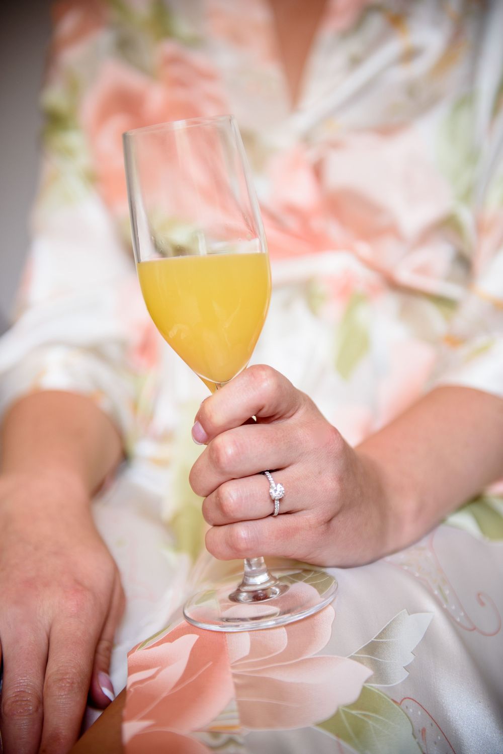 Close up of hands holding mimosa glass showing engagement ring detail.