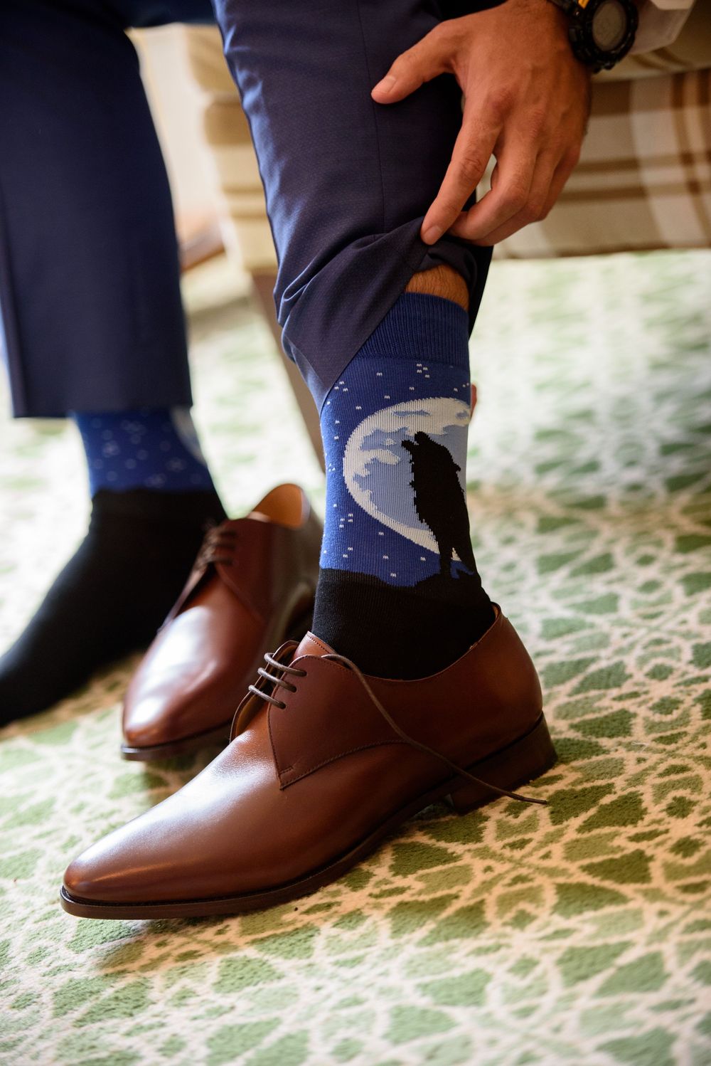 Brown leather dress shoes with polka dot socks on patterned carpet.